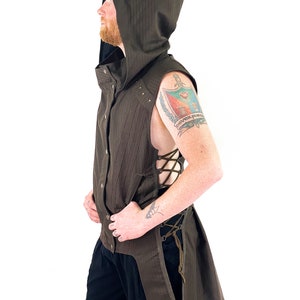 K&ouml;nnte beinhalten: Eine braune &auml;rmellose Weste mit langem Schwanz, einer Kapuze und einem Schn&uuml;rdetail an der Seite. Die Weste hat ein gestreiftes Muster und ist aus einem leichten Stoff gefertigt.