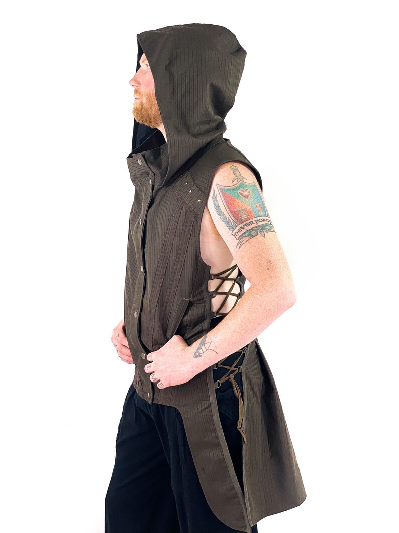 K&ouml;nnte beinhalten: Eine braune &auml;rmellose Weste mit langem Schwanz, einer Kapuze und einem Schn&uuml;rdetail an der Seite. Die Weste hat ein gestreiftes Muster und ist aus einem leichten Stoff gefertigt.