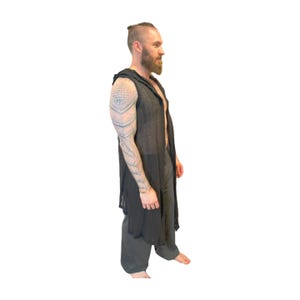 May include: A black hooded vest with a long, open front. The vest is paired with dark gray pants. The outfit is lightweight and appears to be made of a breathable fabric. The model has a beard and tattoos on their arm.