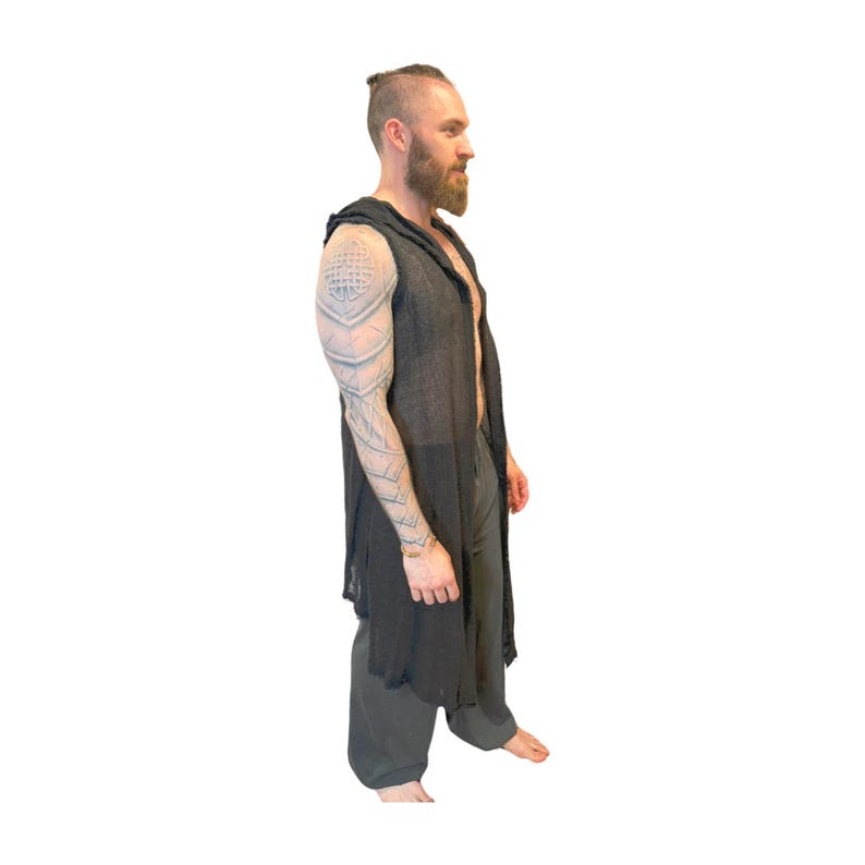 May include: A black hooded vest with a long, open front. The vest is paired with dark gray pants. The outfit is lightweight and appears to be made of a breathable fabric. The model has a beard and tattoos on their arm.