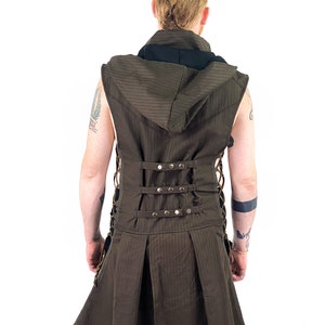 K&ouml;nnte beinhalten: Eine braune &auml;rmellose Weste mit einem schwarzen Kapuzenkragen und einem langen Rock. Die Weste hat ein gestreiftes Muster und ist mit einer Reihe von Metallschnallen und Schn&uuml;ren in der Taille gebunden.