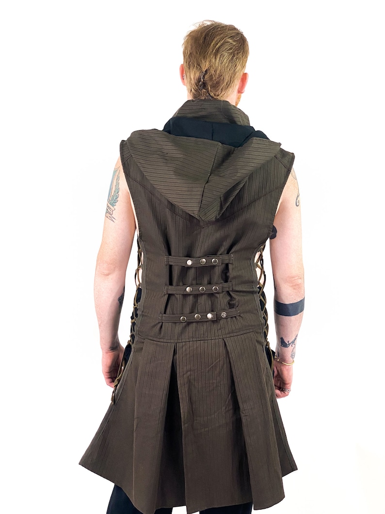 K&ouml;nnte beinhalten: Eine braune &auml;rmellose Weste mit einem schwarzen Kapuzenkragen und einem langen Rock. Die Weste hat ein gestreiftes Muster und ist mit einer Reihe von Metallschnallen und Schn&uuml;ren in der Taille gebunden.