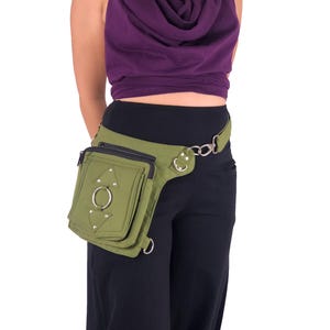 May include: A green canvas fanny pack with silver hardware and a large ring on the front. The fanny pack is worn on a person's hip.