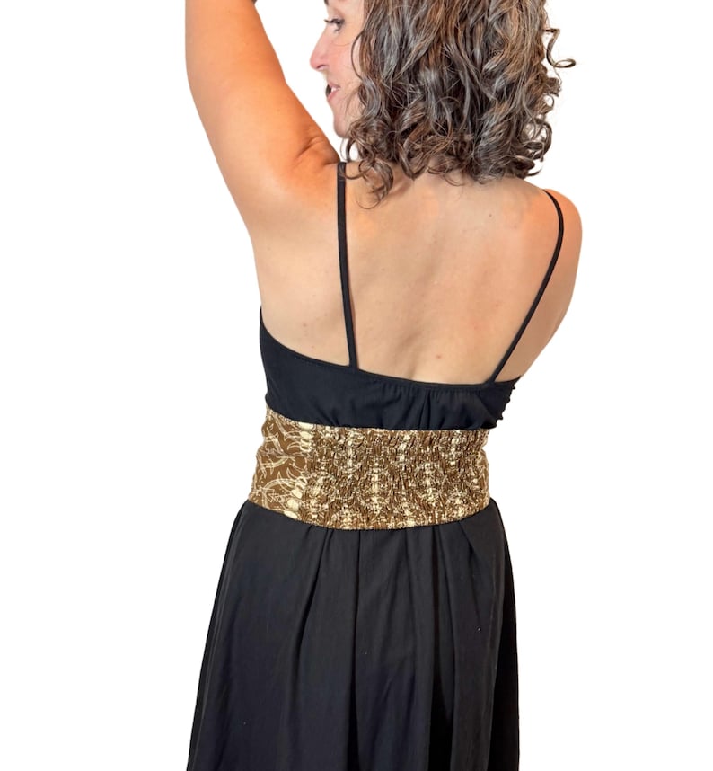 May include: A black dress with spaghetti straps and a wide, gold-colored patterned belt. The dress has a fitted bodice and a flowing skirt. The belt is the focal point, adding a touch of glamour to the simple design.