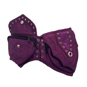 May include: Purple canvas belt with multiple pockets and a lace detail. The belt has metal eyelets and a zipper closure.