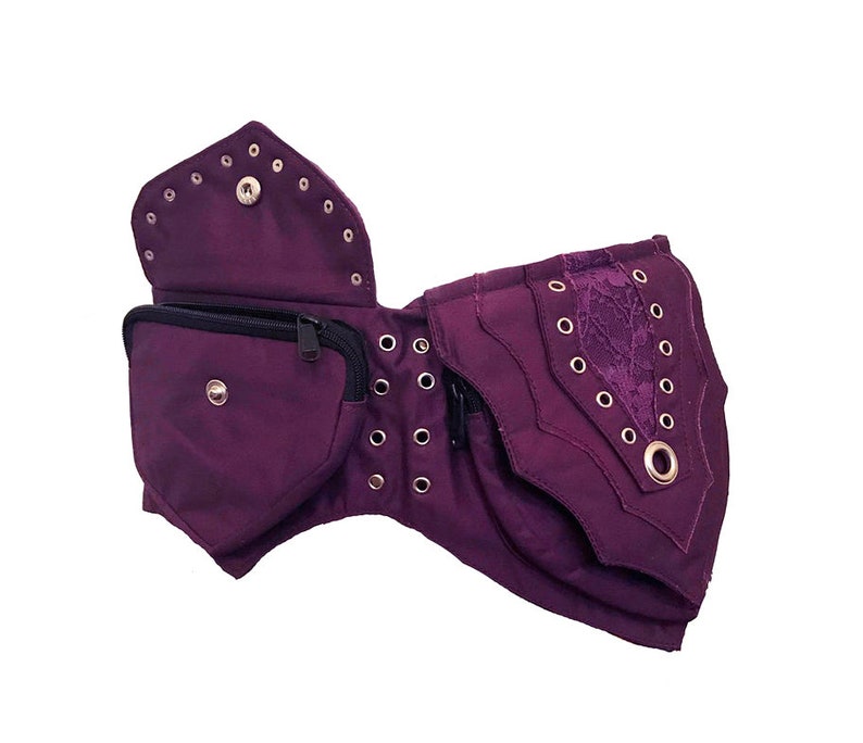 May include: Purple canvas belt with multiple pockets and a lace detail. The belt has metal eyelets and a zipper closure.