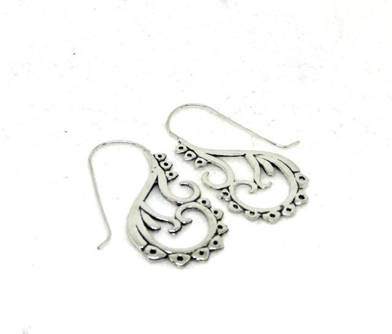 May include: A pair of silver dangle earrings with a delicate, intricate design. The earrings are made of metal and have a filigree pattern.