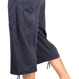May include: Dark blue, knee-length pants with a unique, diamond-shaped pocket detail on the left side. The pants have a drawstring waistband and a tie at the bottom of each leg.