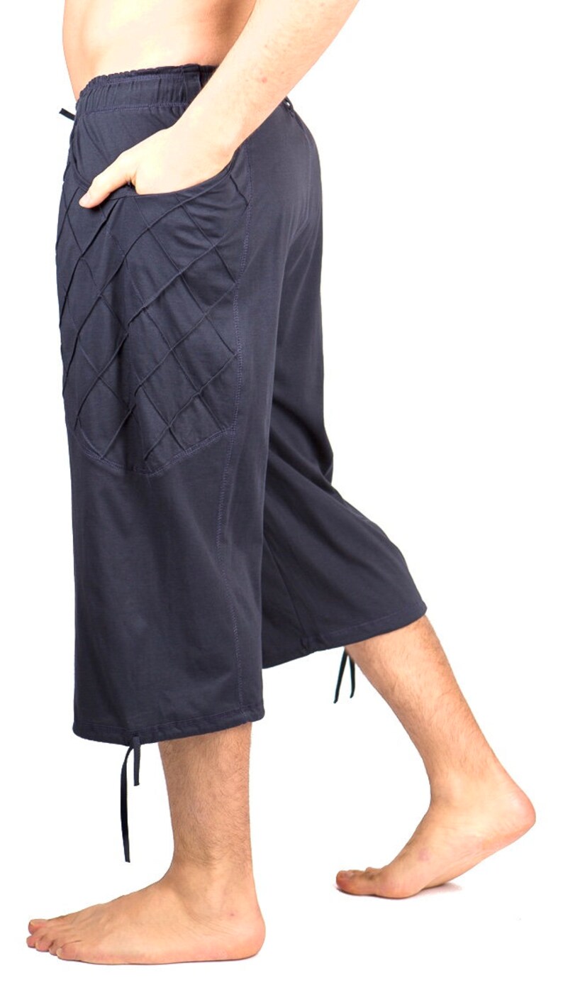 May include: Dark blue, knee-length pants with a unique, diamond-shaped pocket detail on the left side. The pants have a drawstring waistband and a tie at the bottom of each leg.