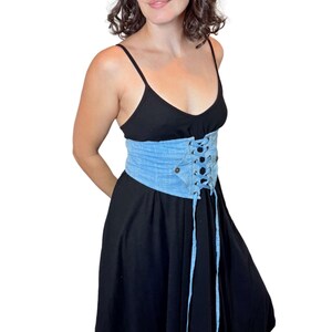 May include: A black dress with spaghetti straps and a light blue denim corset belt. The corset features a lace-up design and a button closure. The dress has a flowing skirt.