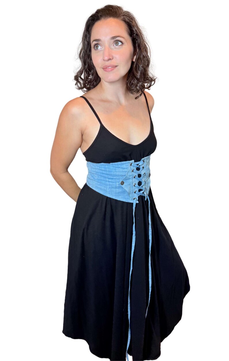 May include: A black dress with spaghetti straps and a light blue denim corset belt. The corset features a lace-up design and a button closure. The dress has a flowing skirt.