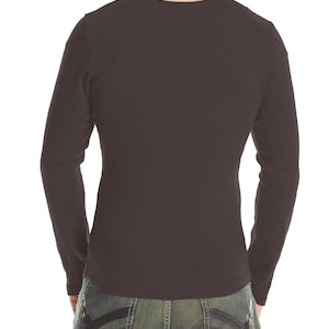 May include: Dark brown long-sleeve shirt with a crew neck. The shirt has a fitted design with seams running down the back. The model is wearing blue denim jeans with decorative stitching on the back pockets.