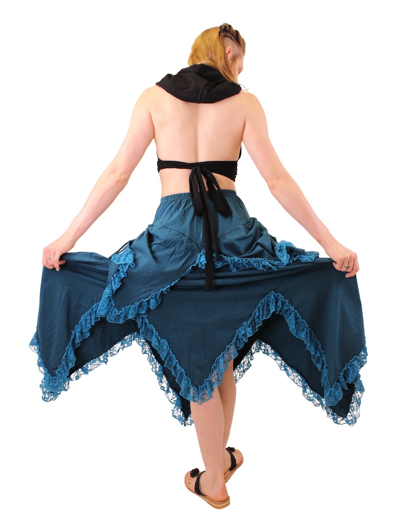 Puede incluir: Una falda azul turquesa con ribete de encaje y un dobladillo con volantes. La falda es asim&eacute;trica y tiene una cintura alta. La falda la lleva puesta una persona con una camiseta negra con capucha.