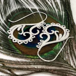 May include: Silver filigree earrings with a delicate, intricate design. The earrings are shaped like a heart with a swirl pattern.