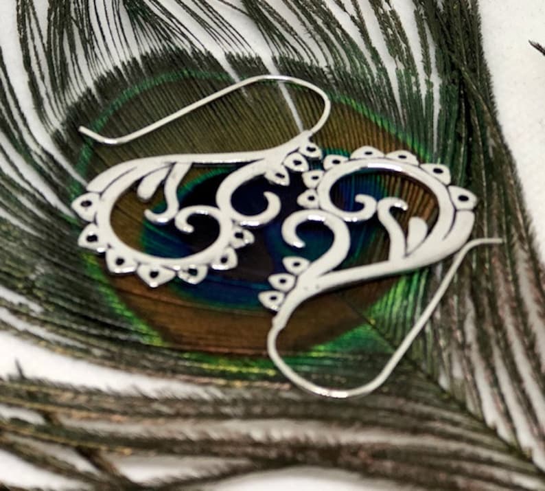 May include: Silver filigree earrings with a delicate, intricate design. The earrings are shaped like a heart with a swirl pattern.
