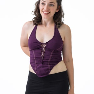 May include: A woman wearing a purple halter top with a lace-up detail and black pants.