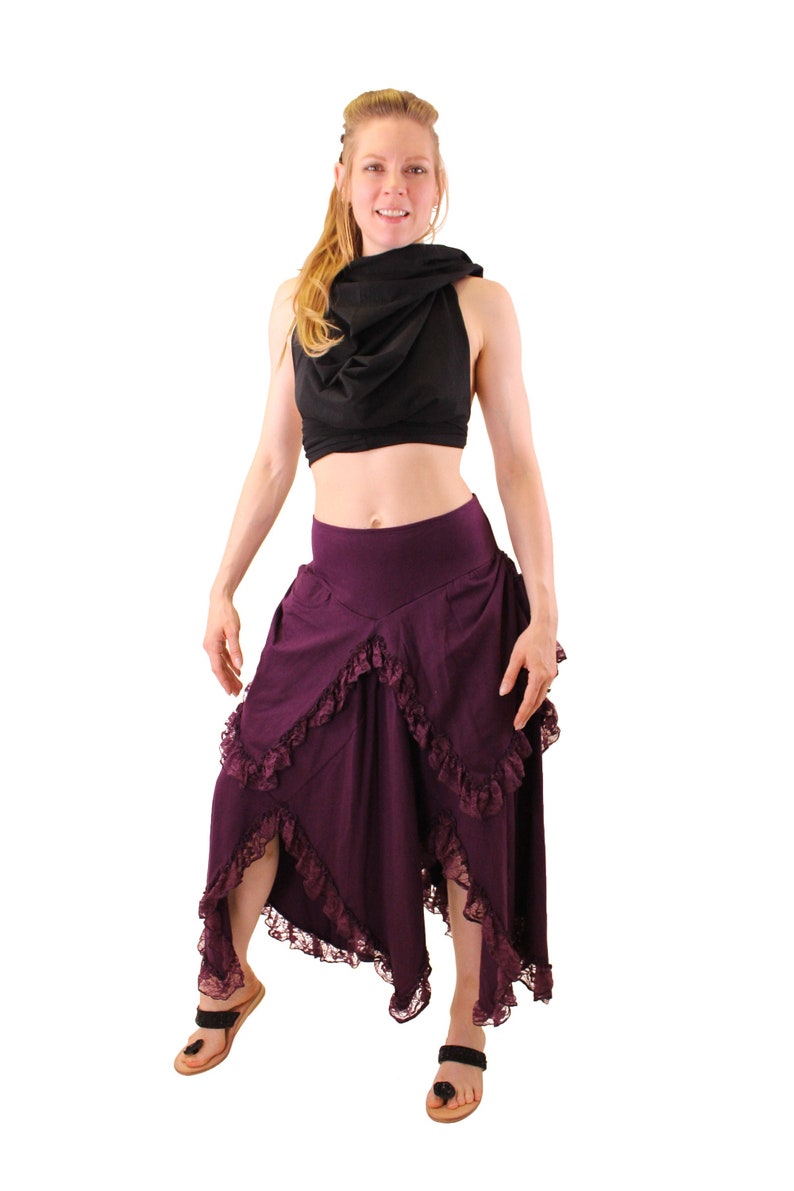 Puede incluir: Una mujer con un top negro corto y una falda larga de color morado con ribete de encaje. La falda es asim&eacute;trica y tiene un dise&ntilde;o fluido.