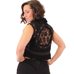 Op de afbeelding: Zwarte, mouwloze vest met een gehaakt ontwerp en een kantpaneel op de rug. De vest heeft een hoge halslijn en een gerimpelde zoom.