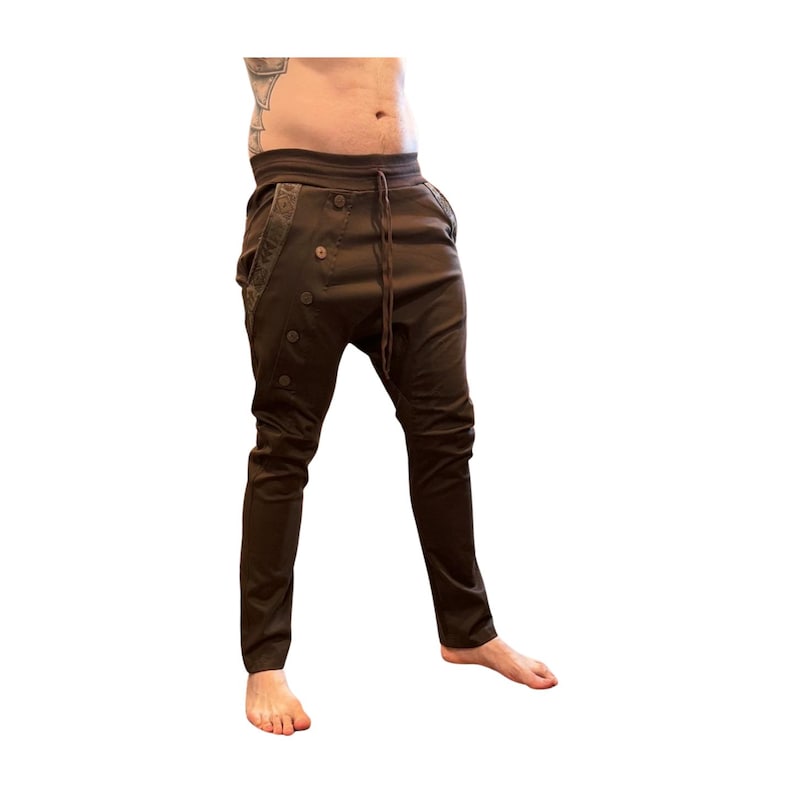 Puede incluir: Pantalones marrones con cintura con cord&oacute;n y detalles de botones. Los pantalones tienen un ajuste relajado en la parte superior y se estrechan en las piernas. Los pantalones son de un material suave.