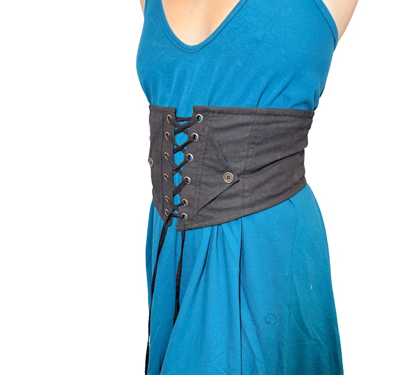 May include: A black corset belt with a lace-up front and a button closure. The belt is worn over a blue dress. The corset belt is made of a sturdy material and has a structured design.