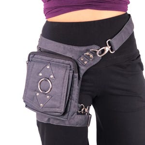 May include: A gray canvas thigh bag with a large silver ring and silver studs. The bag is attached to a gray canvas belt with a silver buckle and a silver clip.