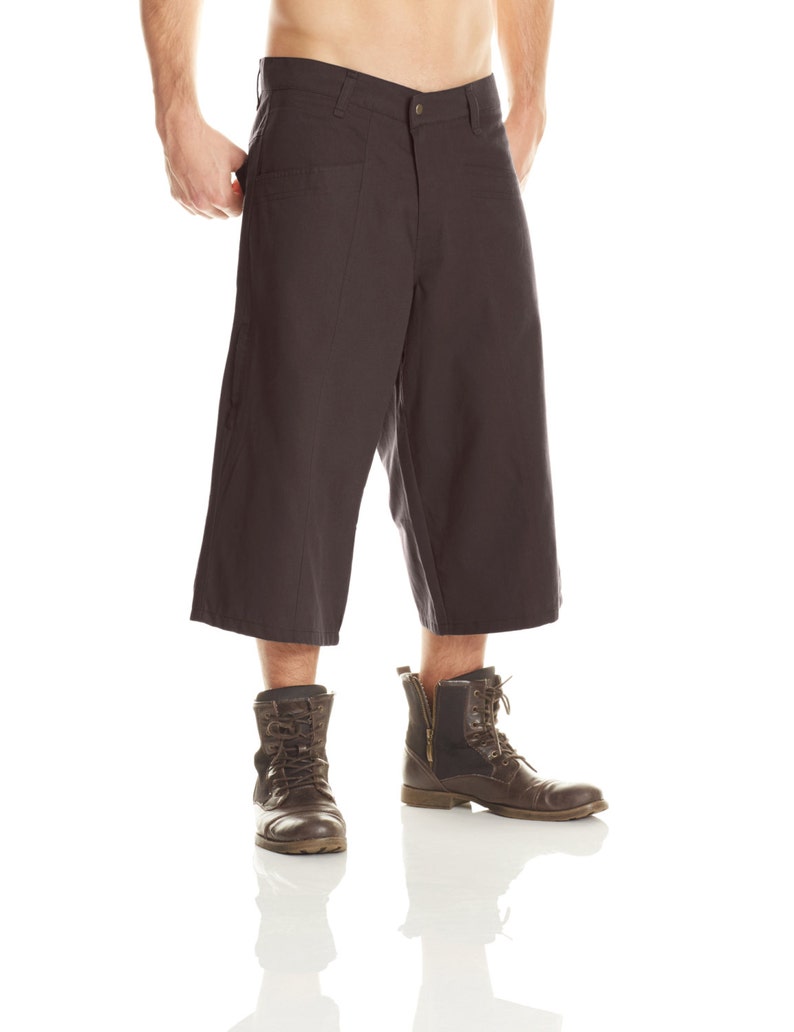 May include: A pair of dark gray cuffed pants with a zipper fly and button closure. The pants are worn by a person wearing brown leather boots.
