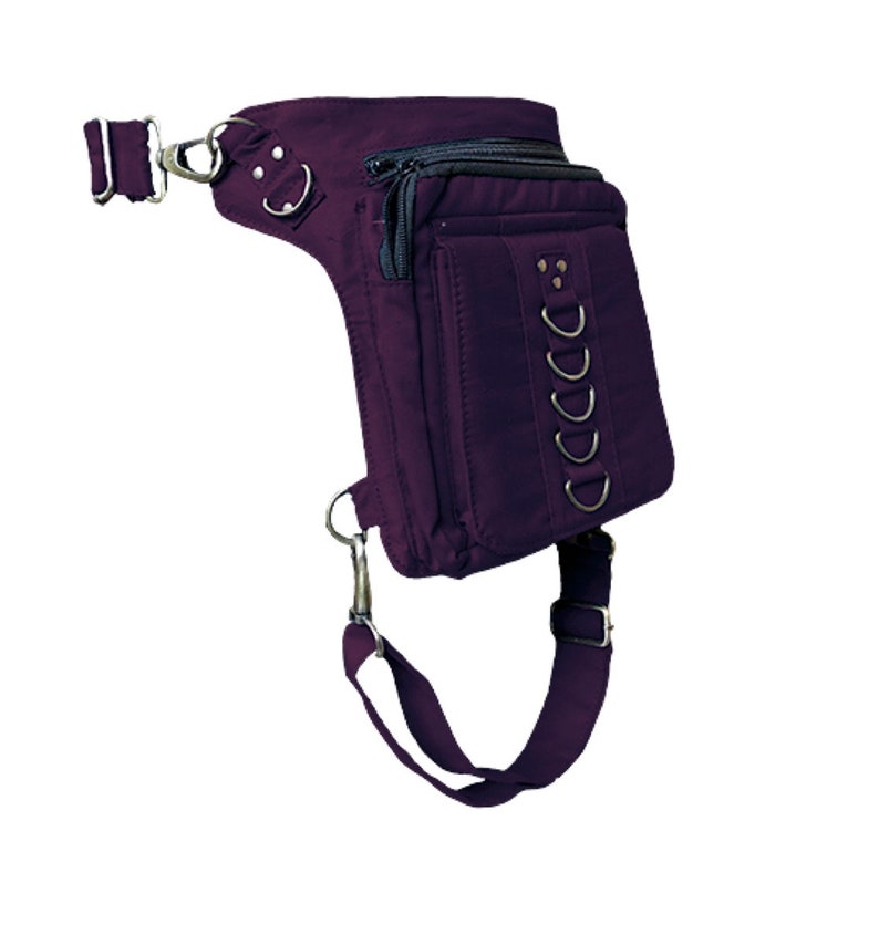 May include: A purple canvas thigh bag with multiple pockets and a strap. The bag has a zipper closure and metal accents.