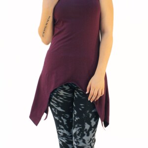 May include: A woman wearing a purple hooded tunic with a high-low hemline and black and gray patterned leggings. She is barefoot and has teal blue hair.