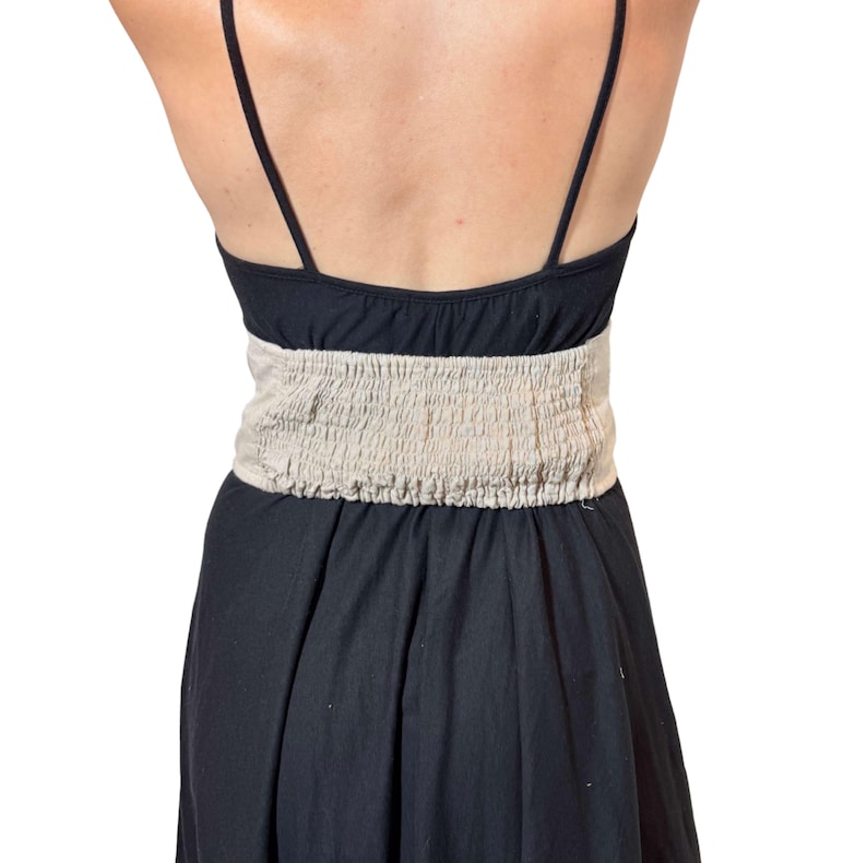 May include: Black sundress with spaghetti straps and a beige, ruched waistband. The skirt of the dress is flared and flows down from the waist. The dress is made of a soft, lightweight fabric.