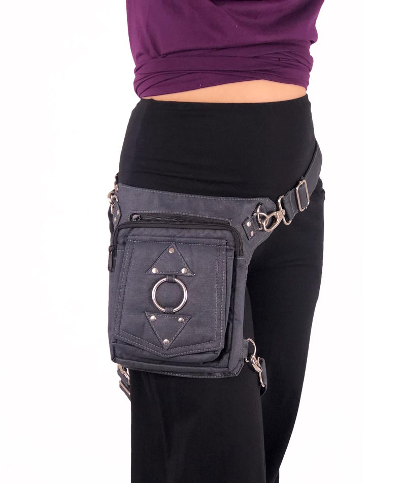 May include: A gray canvas thigh bag with a zippered pocket, a metal ring, and silver studs. The bag is worn on a person's right thigh and is secured with a belt.