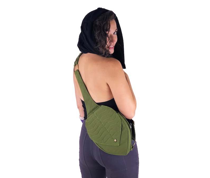May include: A woman wearing a black top and dark grey pants with a green leaf-shaped crossbody bag.