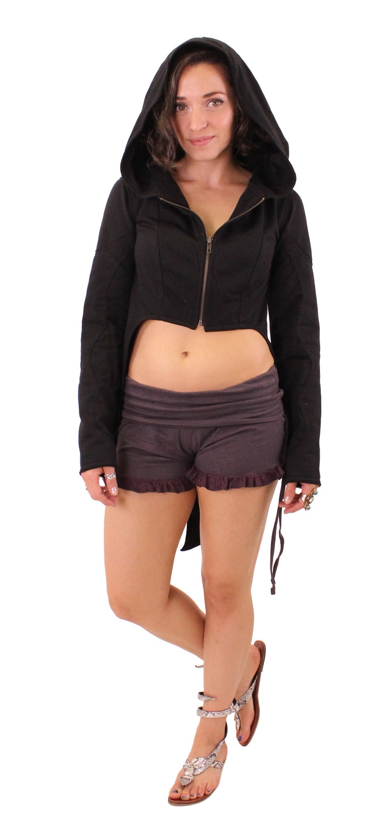 May include: A black hooded cropped jacket with a long back tail and a zipper closure. The jacket is worn over a pair of dark brown shorts with a ruffled hem.