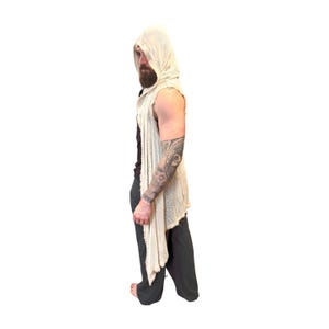 May include: A sleeveless, hooded vest in a light beige color. The vest has a draped, asymmetrical design with a raw hem. The garment is made of a lightweight, textured fabric. The model is wearing dark gray pants.