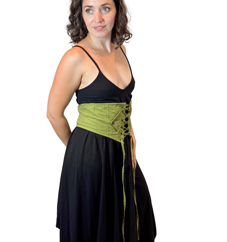 May include: A black dress with a green corset-style belt. The belt is a light green color and features a lace-up design in the front. The dress has a simple, sleeveless top and a flowing skirt.