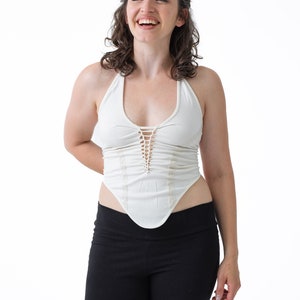 May include: A woman wearing a white halter top with a lace trim and black leggings. She is smiling and looking up.