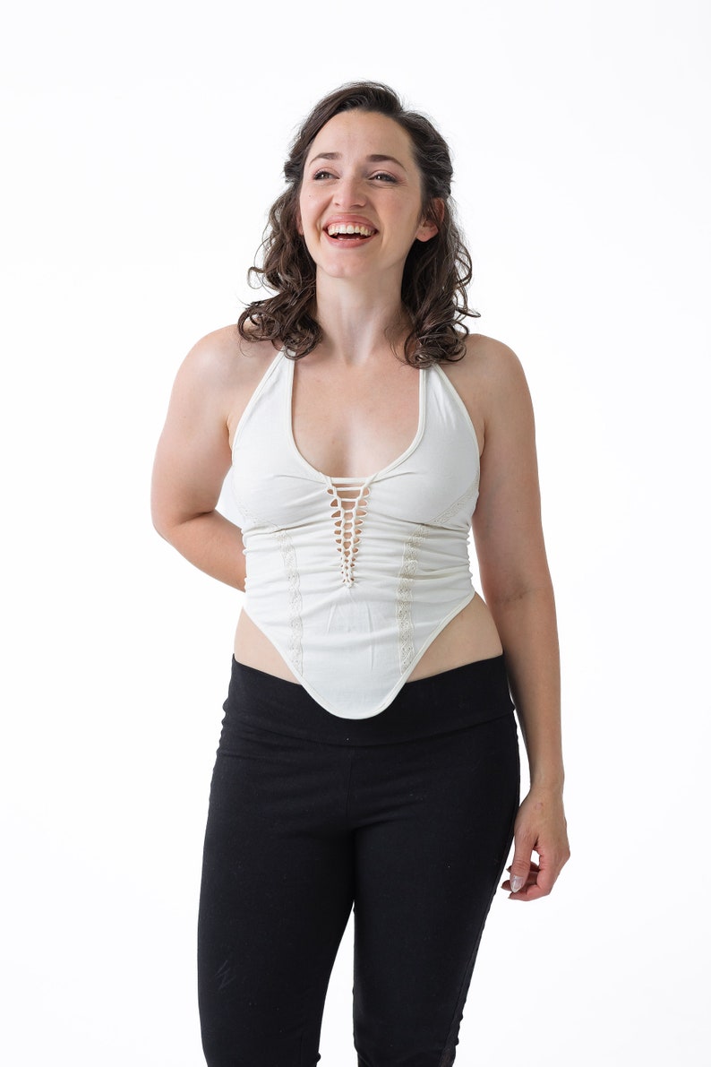 May include: A woman wearing a white halter top with a lace trim and black leggings. She is smiling and looking up.
