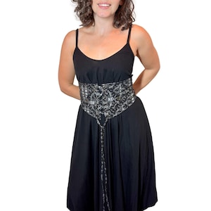 May include: A black dress with spaghetti straps and a decorative corset-style belt. The belt features a silver and black pattern with eyelets and a tie closure. The dress has a flowing skirt.