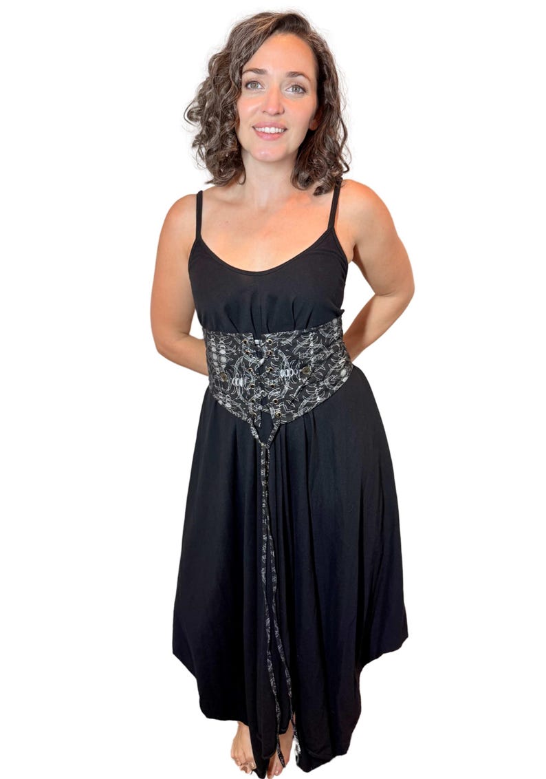 May include: A black dress with spaghetti straps and a decorative corset-style belt. The belt features a silver and black pattern with eyelets and a tie closure. The dress has a flowing skirt.