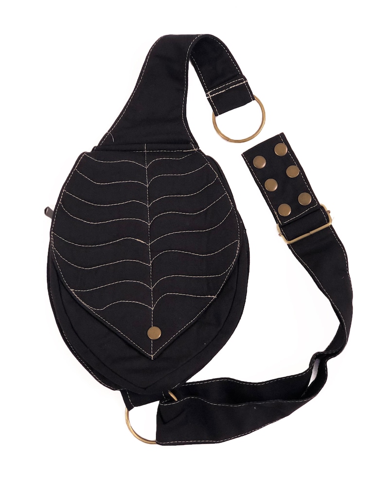 May include: A black canvas crossbody bag with a unique leaf-shaped design and a decorative stitched pattern. The bag has a long adjustable strap with brass hardware and a small zippered pocket.