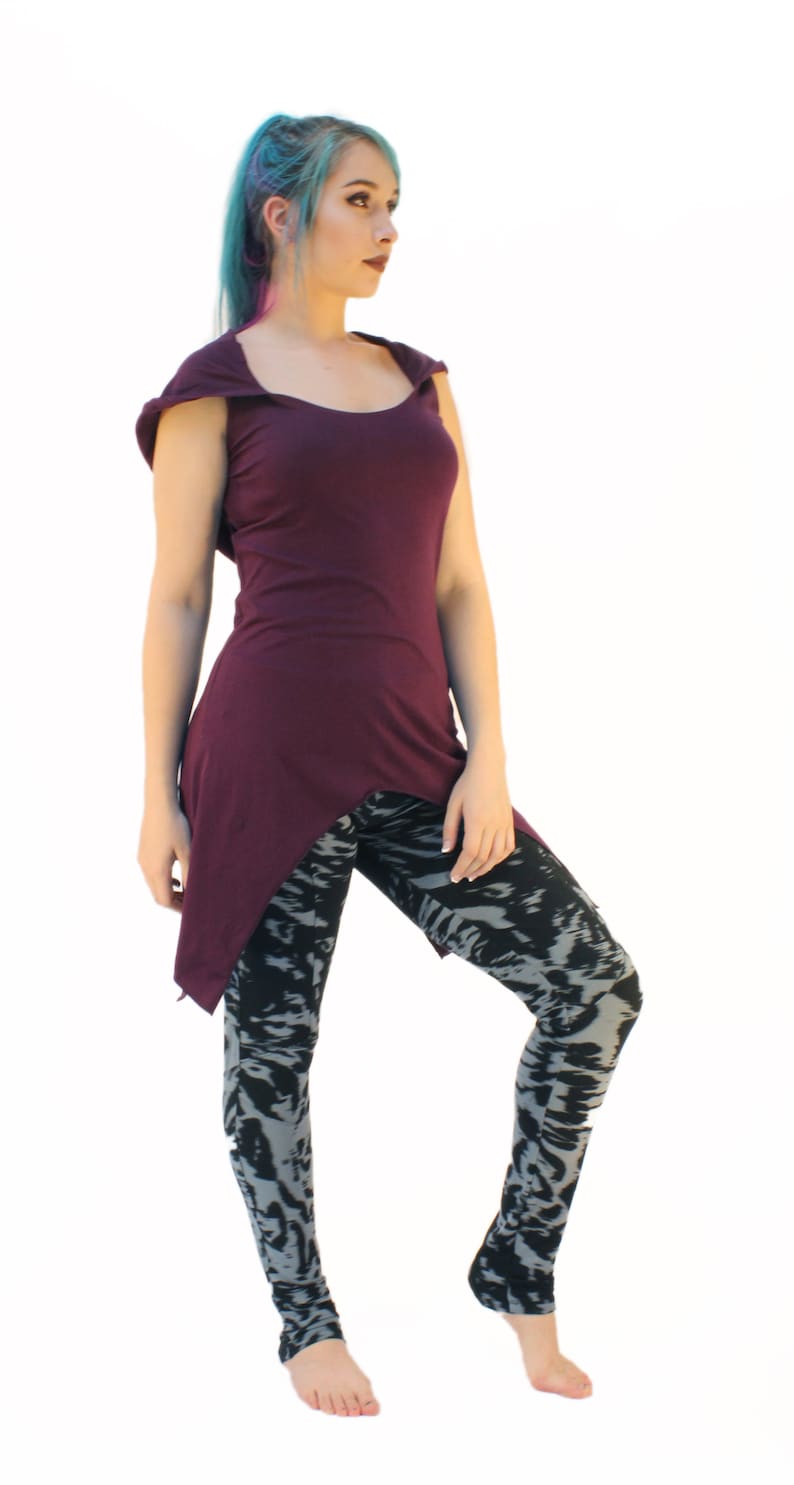 May include: A woman wearing a purple asymmetrical top with a scoop neck and black and gray patterned leggings.