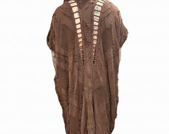 May include: A brown hooded cloak with a distressed, textured design. The back features vertical cut-out details and a patchwork pattern. The cloak has short sleeves and a long, flowing hemline. The garment is made of a soft, possibly woven material.