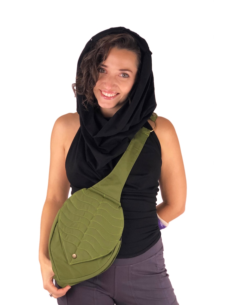 May include: A woman wearing a black cowl neck top and a black scarf is carrying a green leaf-shaped crossbody bag with a quilted design.