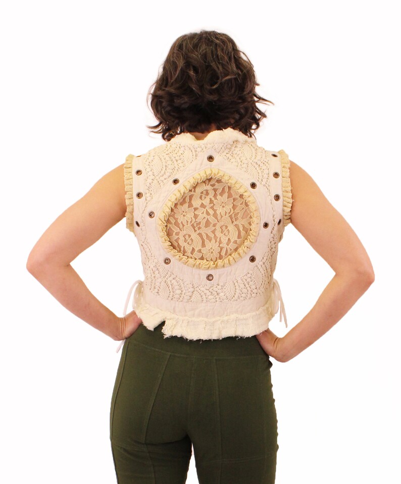 Op de afbeelding: Een wit gehaakt vest met een achterpaneel van kant en een bruine leren bies. Het vest heeft een getailleerde lengte en een gerimpelde zoom.
