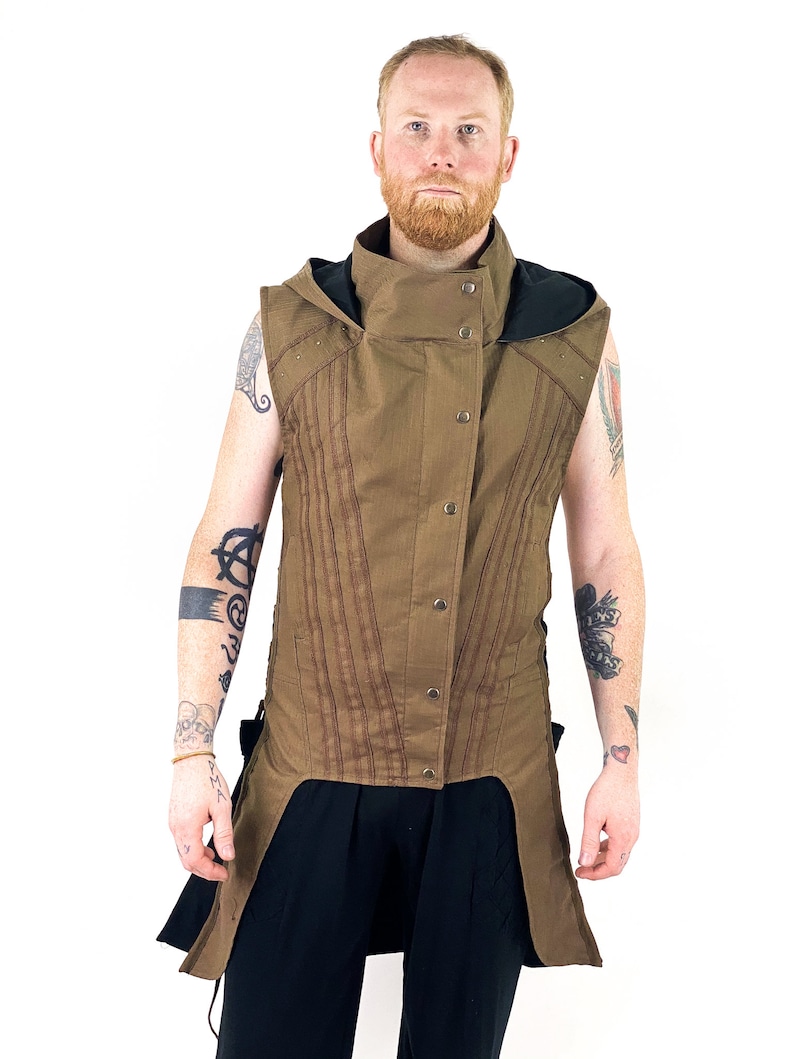 K&ouml;nnte beinhalten: Eine braune &auml;rmellose Weste mit hohem Kragen und einer schwarzen Kapuze. Die Weste hat einen langen, spitzen Saum und wird mit Kn&ouml;pfen geschlossen. Die Weste ist aus einem strukturierten Stoff gefertigt und hat einen l&auml;ssigen, entspannten Stil.