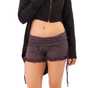 May include: A black hooded jacket with a long back and a short front, worn with dark gray shorts and snake-skin sandals.