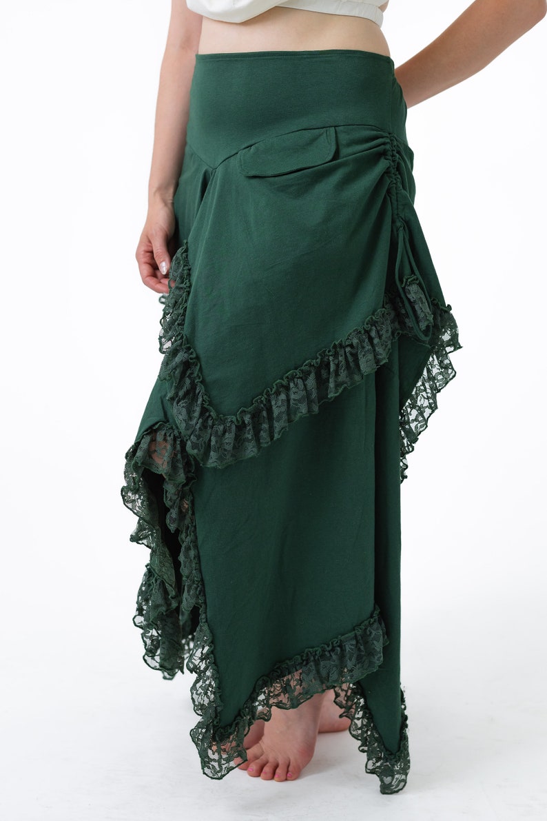 Puede incluir: Una falda larga de color verde oscuro con ribete de encaje. La falda tiene un detalle fruncido en la parte posterior y un bolsillo en el lado derecho.