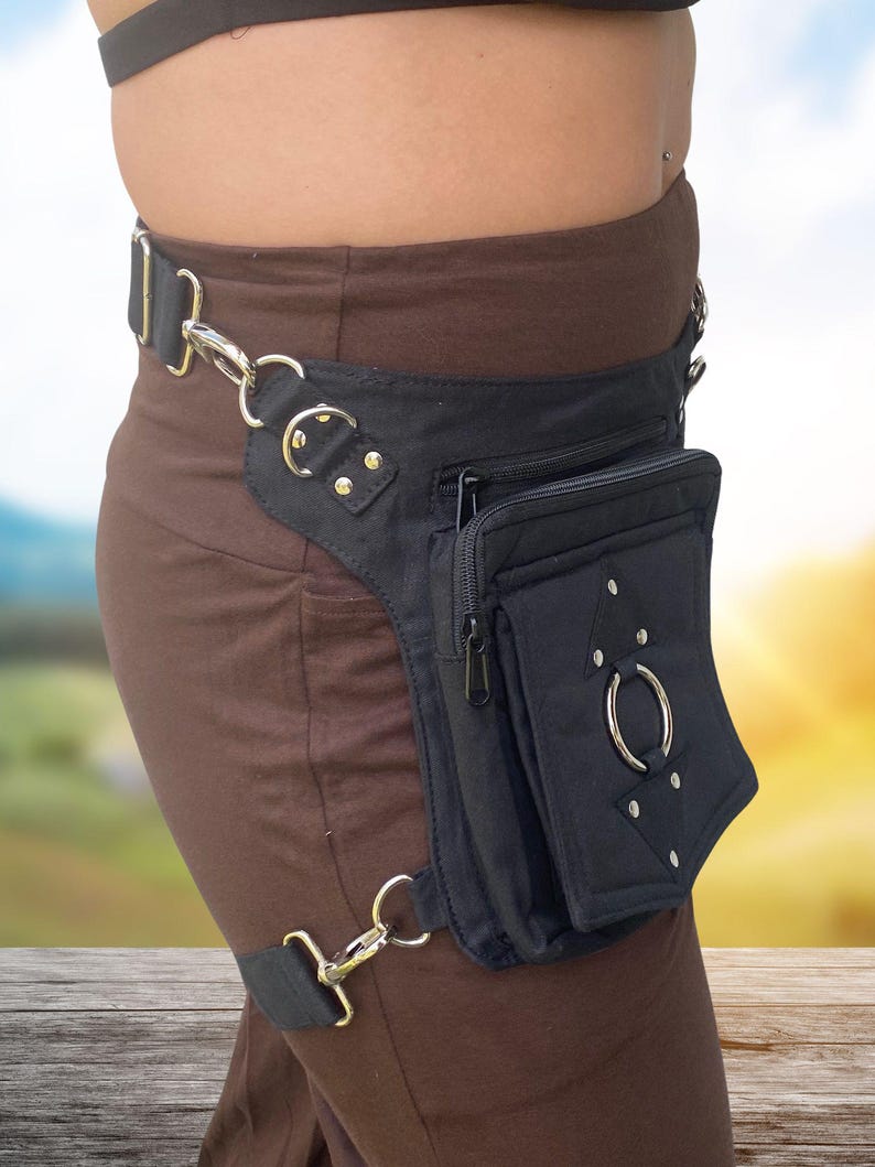 May include: A black canvas fanny pack with a zippered pocket and a large metal ring. The fanny pack is worn on the hip and has a strap that goes around the leg.