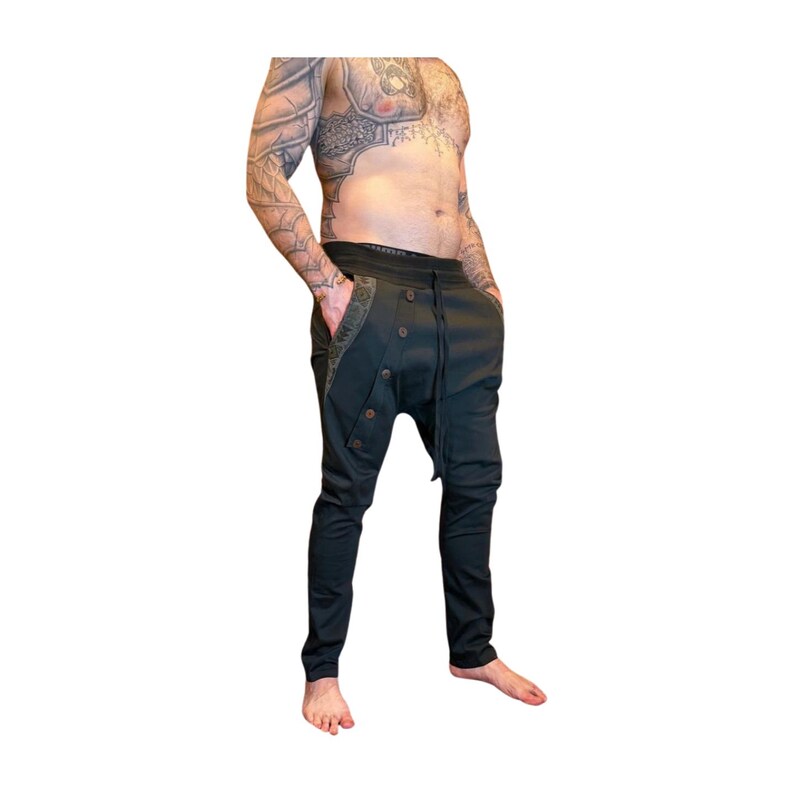 Puede incluir: Pantalones negros con un dise&ntilde;o &uacute;nico. Los pantalones tienen una bragueta abotonada, bolsillos con costuras decorativas y una cintura con cord&oacute;n. Los pantalones tienen un ajuste relajado en las caderas y una pernera c&oacute;nica.