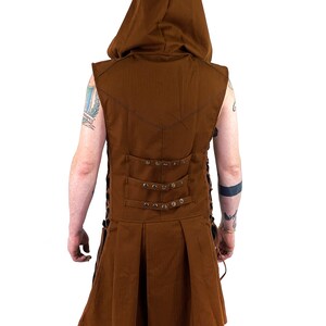 K&ouml;nnte beinhalten: Eine braune &auml;rmellose Kapuzenweste mit einem langen, flie&szlig;enden Rock. Die Weste hat einen Schn&uuml;rr&uuml;cken mit Metallverzierungen und einen spitzen Kragen.