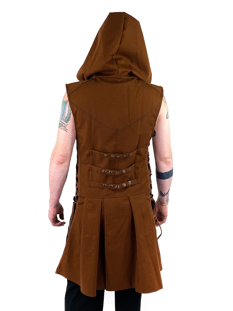 K&ouml;nnte beinhalten: Eine braune &auml;rmellose Kapuzenweste mit einem langen, flie&szlig;enden Rock. Die Weste hat einen Schn&uuml;rr&uuml;cken mit Metallverzierungen und einen spitzen Kragen.